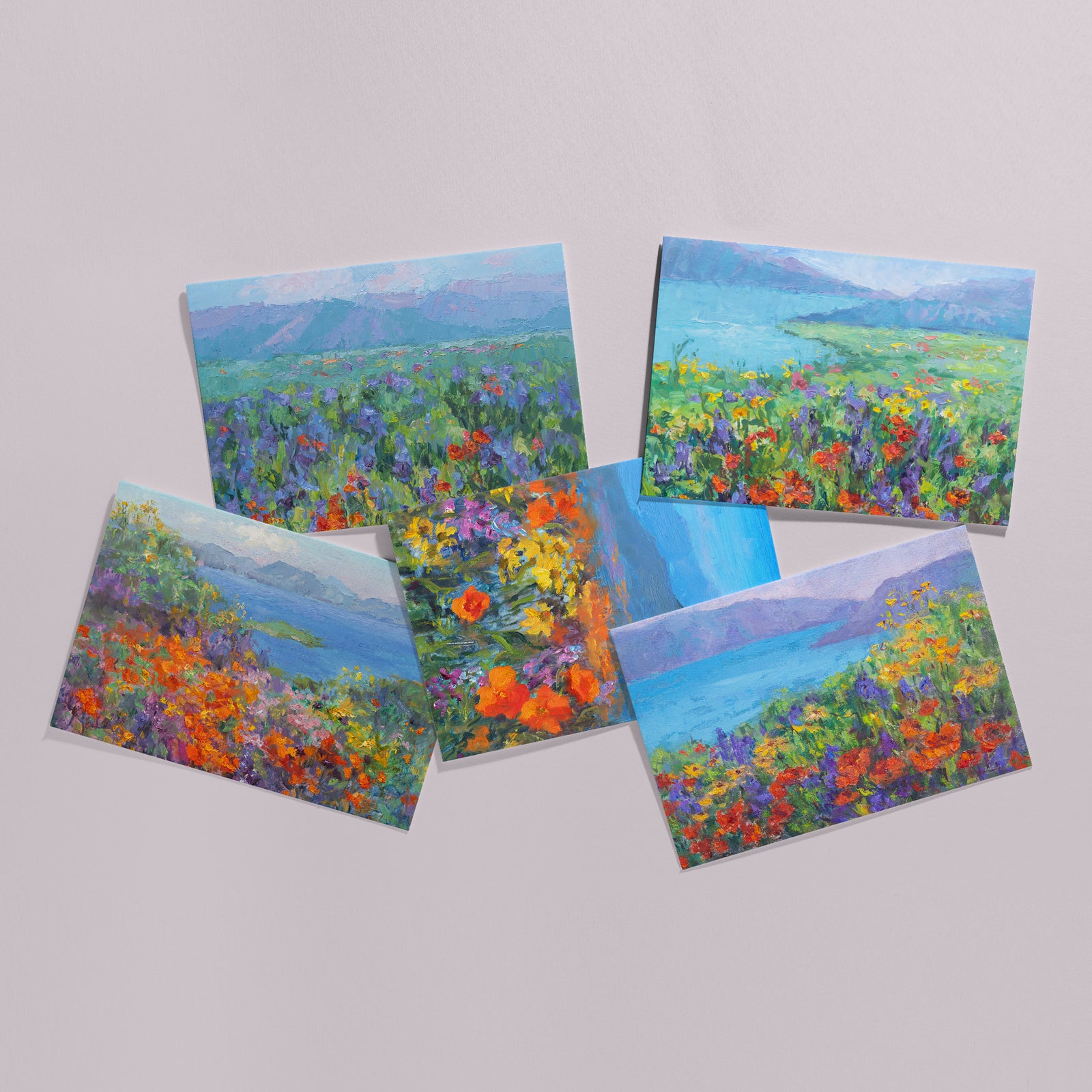 Fine art greeting card set 5x7, five cards displayed on background, including orange California poppies and other wildflowers, meadows, hills, lake, all based on original landscape oil paintings by Oksana Johnson. Yellow flowers, green grass, blue water, white clouds.