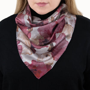 Woman wearing a square silk scarf with floral pattern in red, berry, maroon, and light colors, hand-hemmed edges, and a black sweater. 