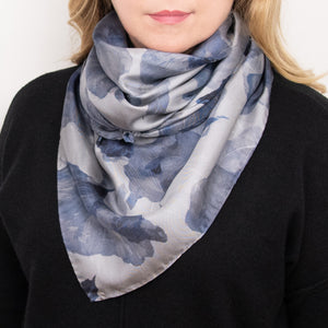 Woman wearing a silk scarf with overlapping floral images in blue tones, and hand-hemmed edges, along with a black top. 