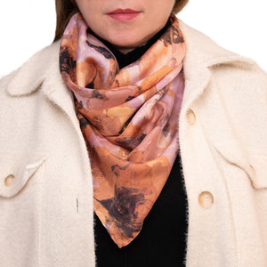Woman wearing a medium-sized silk scarf in a floral pattern with orange flowers and hand hemmed edges, along with a white coat and a black top. 