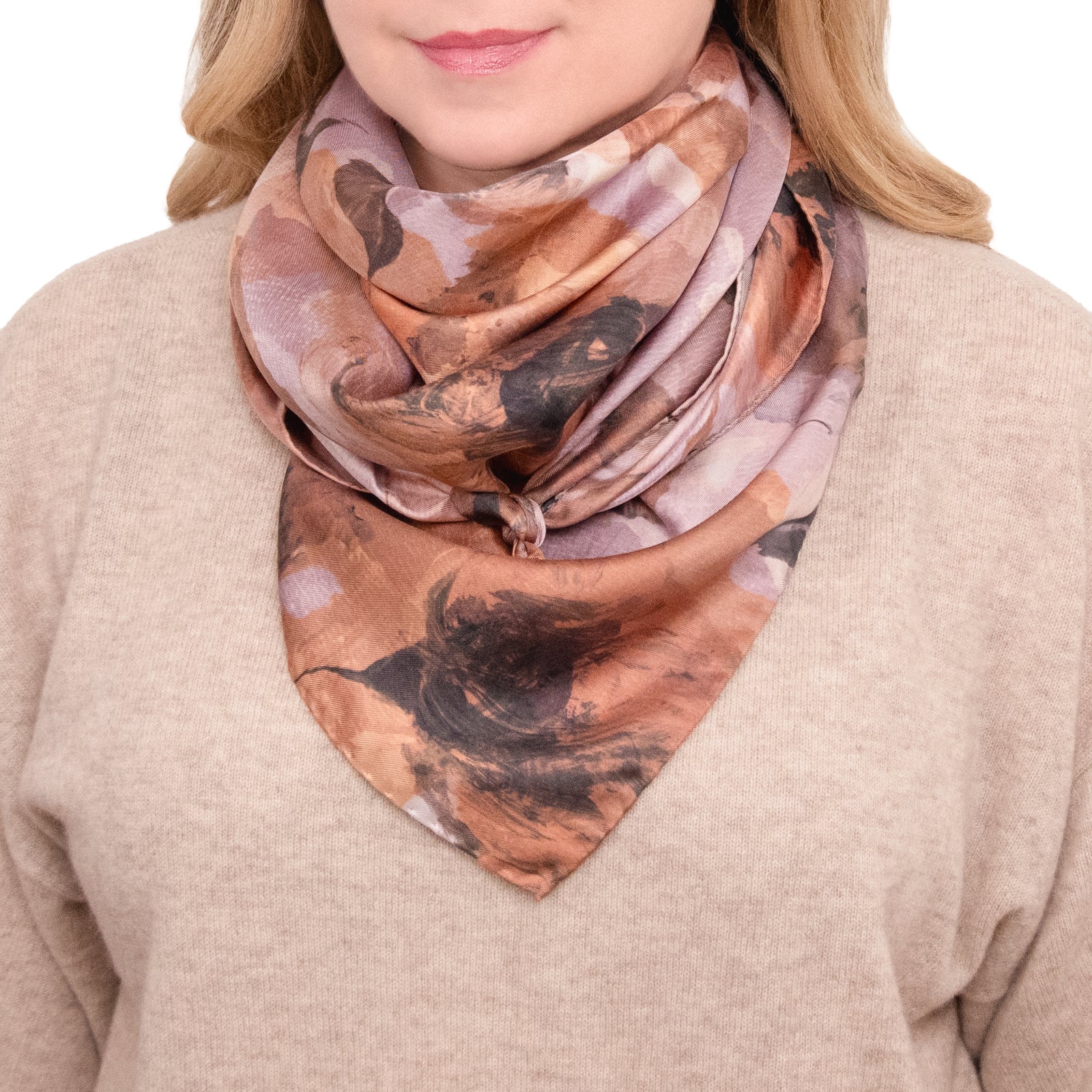 Woman wearing floral scarf in peach, rose, and coral tones, with light sweater.