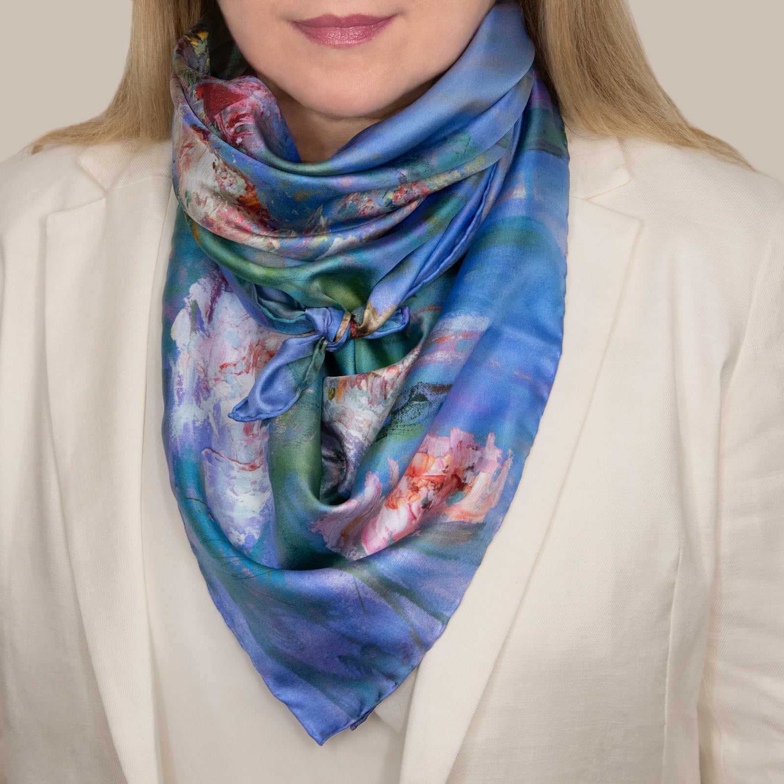 Woman in a cream blazer wearing a Floating Nympheas silk scarf tied in front, showing white and pink waterlily blossoms on a field of blue and green. 