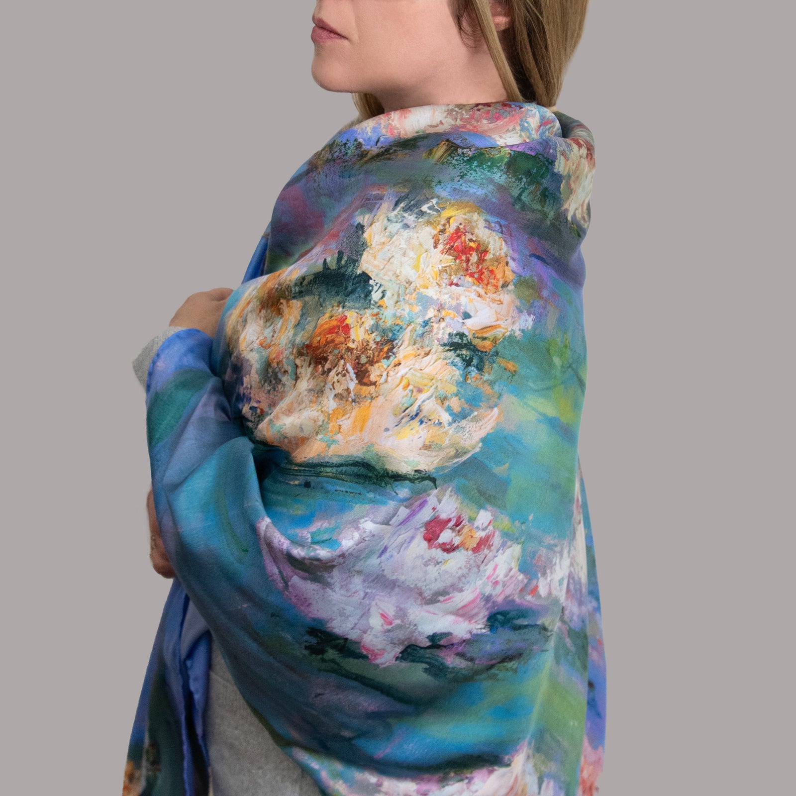 Woman in profile wearing a very large Floating Nympheas silk scarf around her shoulders, showing impressionistic yellow and pink water lily blossoms on a field of green and blue. 