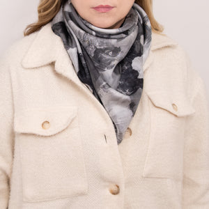Woman wearing a silk scarf in a floral pattern with black, white, and gray overlapping images and hand hemmed edges, along with a white coat. 