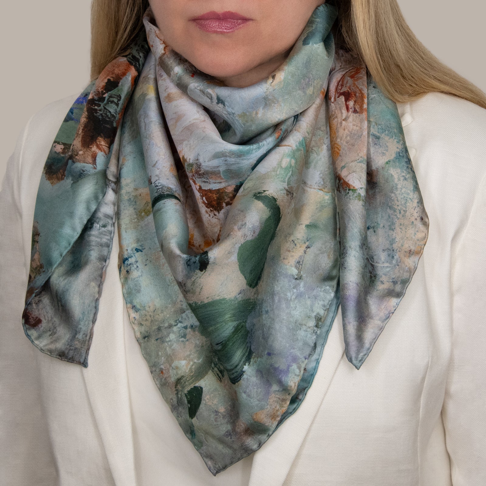 Woman in a white jacket and top wearing a large silk scarf, with impressionist design in various shades of green, brown, and light colors.