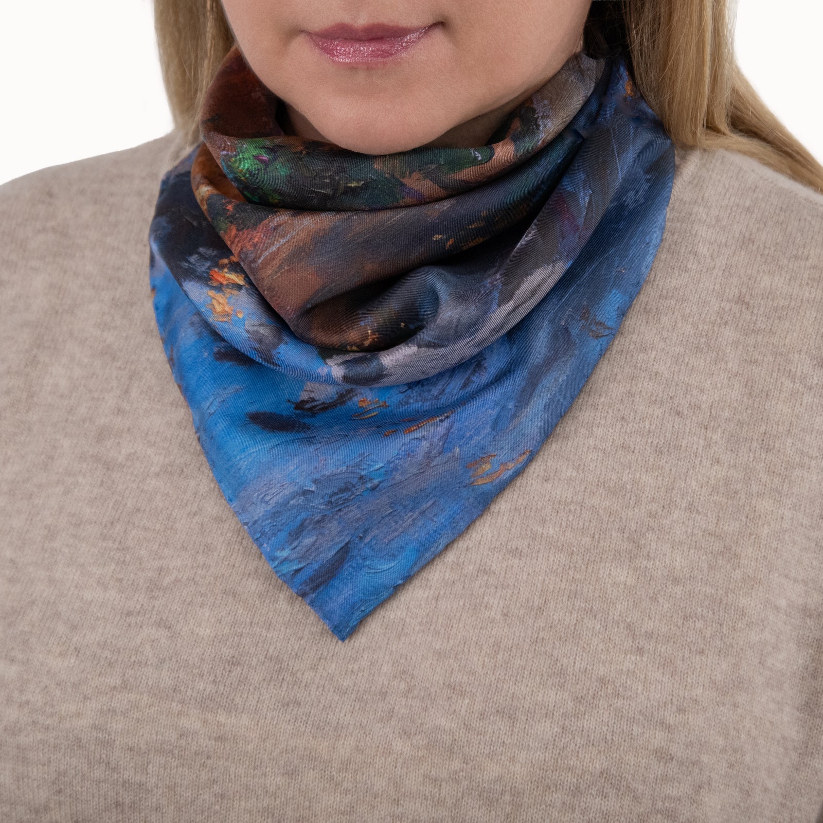 Woman wearing a square silk scarf based on painting of Italian lakeside scene with boats and buildings at dusk, against a beige sweater.