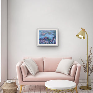 Irises and Waterlilies, archival fine art print by Oksana Johnson shown in a living room above a pink sofa with white pillows and a table— deep purple and mauve irises in the foreground, calm blue water and floating lilies beyond