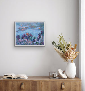 Irises and Waterlilies, archival fine art print by Oksana Johnson shown on wall above a wooden cabinet with a vase and other items— deep purple and mauve irises in the foreground, calm blue water and floating lilies beyond