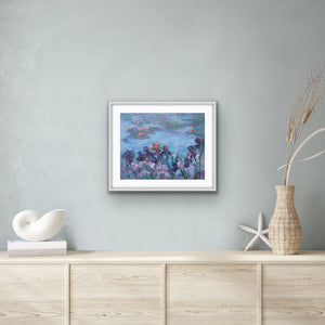 Irises and Waterlilies, archival fine art print by Oksana Johnson shown on a wall above a wooden cabinet with decorative items— deep purple and mauve irises in the foreground, calm blue water and floating lilies beyond