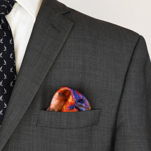 Oksana's Orange Bouquet 16.5-inch scarf styled as a men's pocket square in a gray suit with a blue tie.