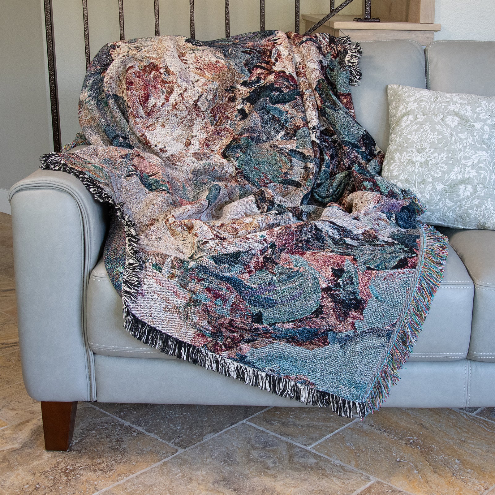 Floral patterned decorative woven blanket with impressionist design of roses, draped over a couch, in front of stairs.
