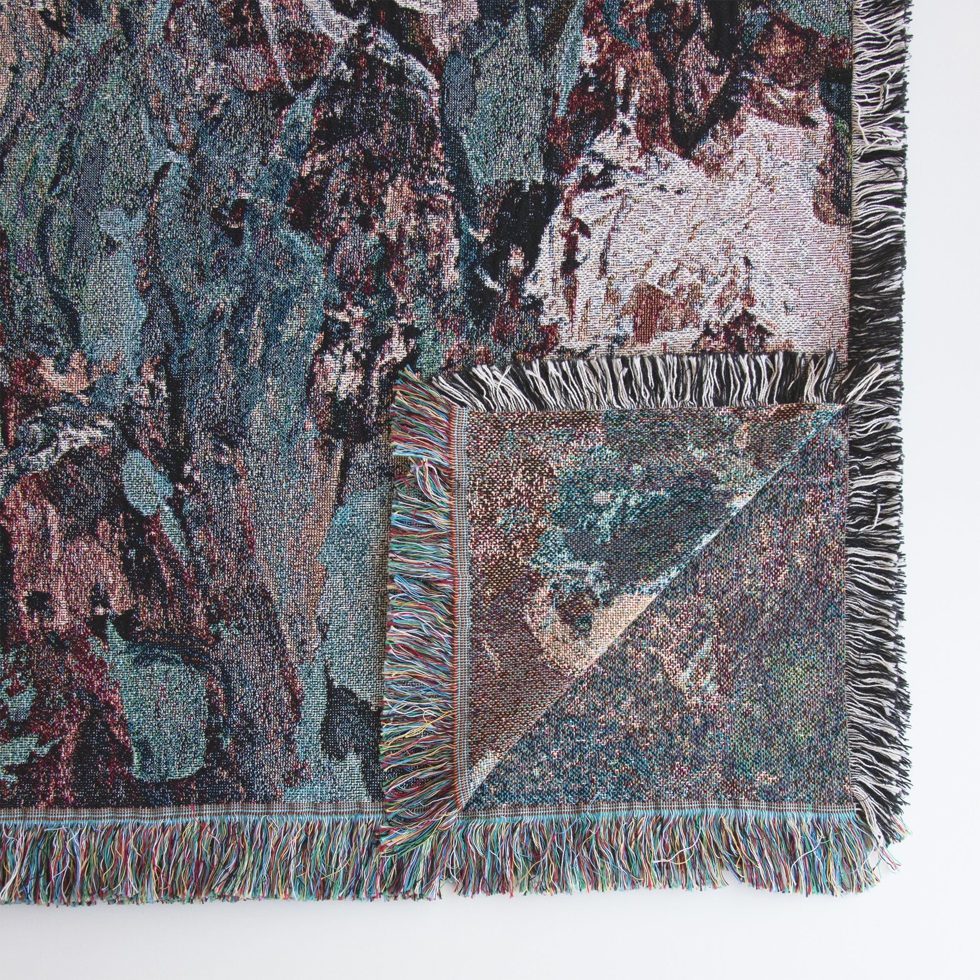 Close-up of lower right corner of decorative floral blanket with impressionist design, showing upturned corner with back side of image that is woven into the fabric itself. 