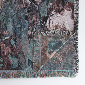 Close-up of lower right corner of decorative floral blanket with impressionist design, showing upturned corner with back side of image that is woven into the fabric itself. 