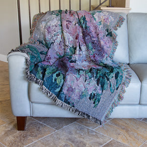 Fine art woven blanket with pink and violet rose blossoms in an impressionist style, draped over a couch, against a backdrop of stairs.