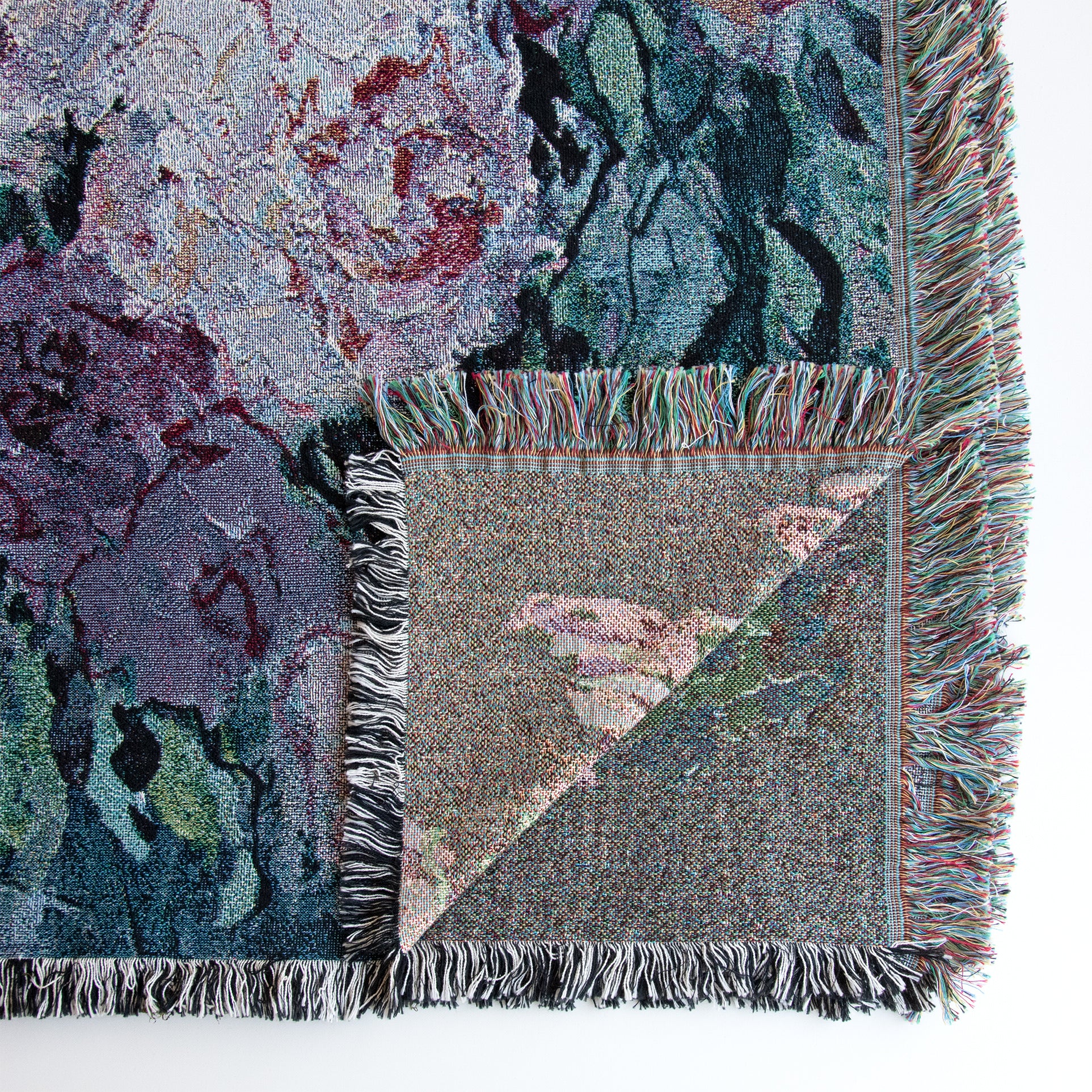 Close-up of lower right corner of fine art decorative blanket, overturned, showing part of the back side design of floral image and fringed edges. 