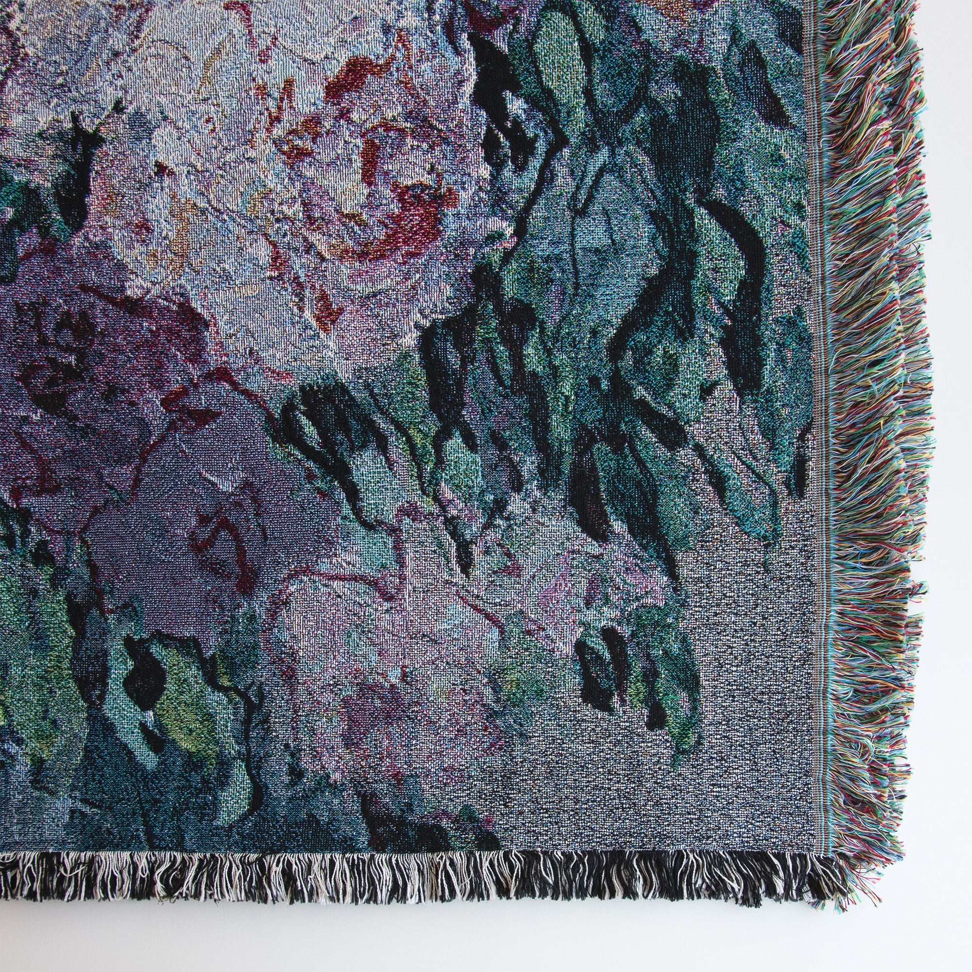 Close-up of lower right corner of fine art decorative blanket, showing floral design, details of the weave, and fringed edges in multiple colors and black and white. 