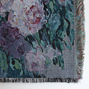 Close-up of lower right corner of fine art decorative blanket, showing floral design, details of the weave, and fringed edges in multiple colors and black and white. 