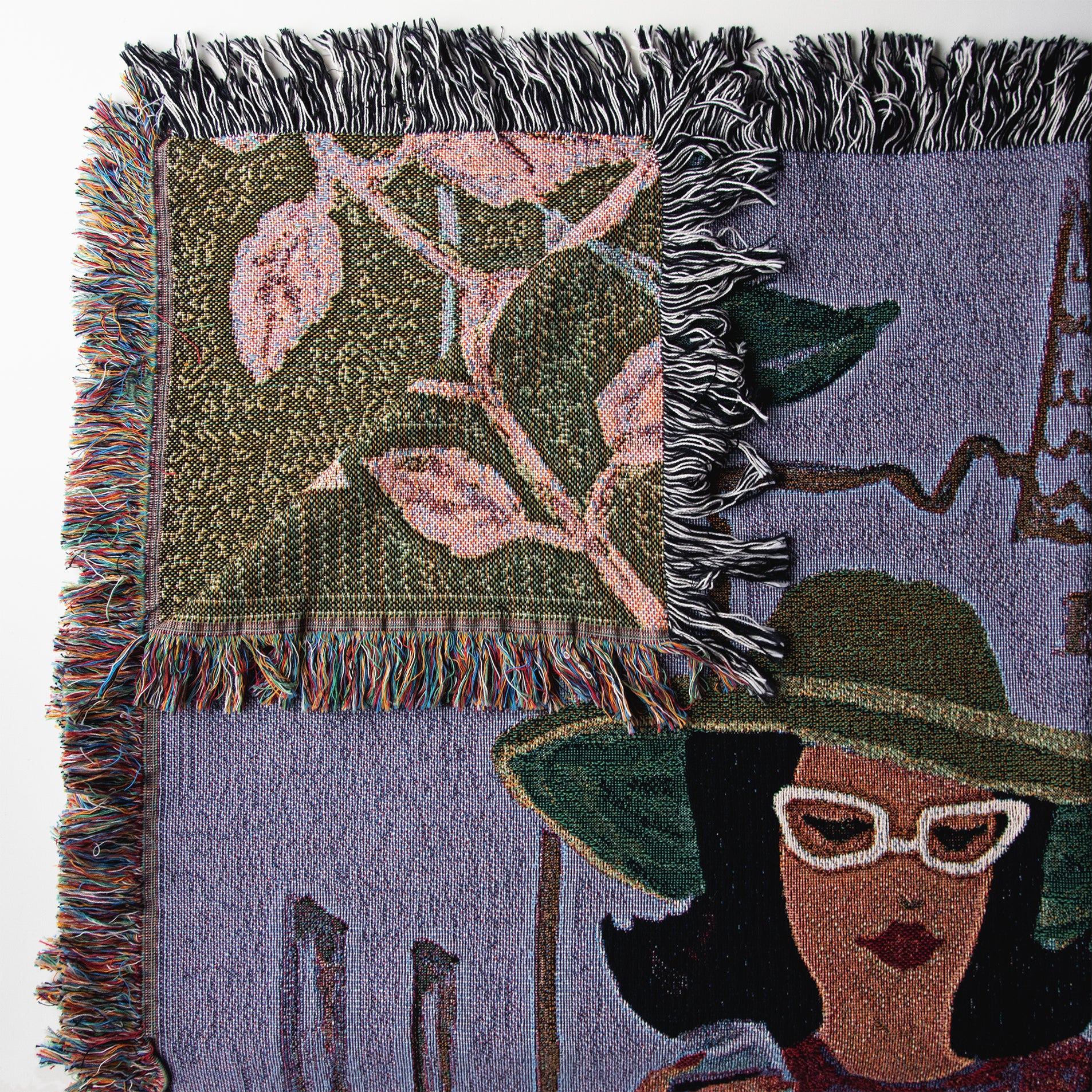 Details from upper left hand corner of a woven blanket folded over, showing part of the back side image woven into the fabric, next to the main front side image of the woman in a hat and glasses.
