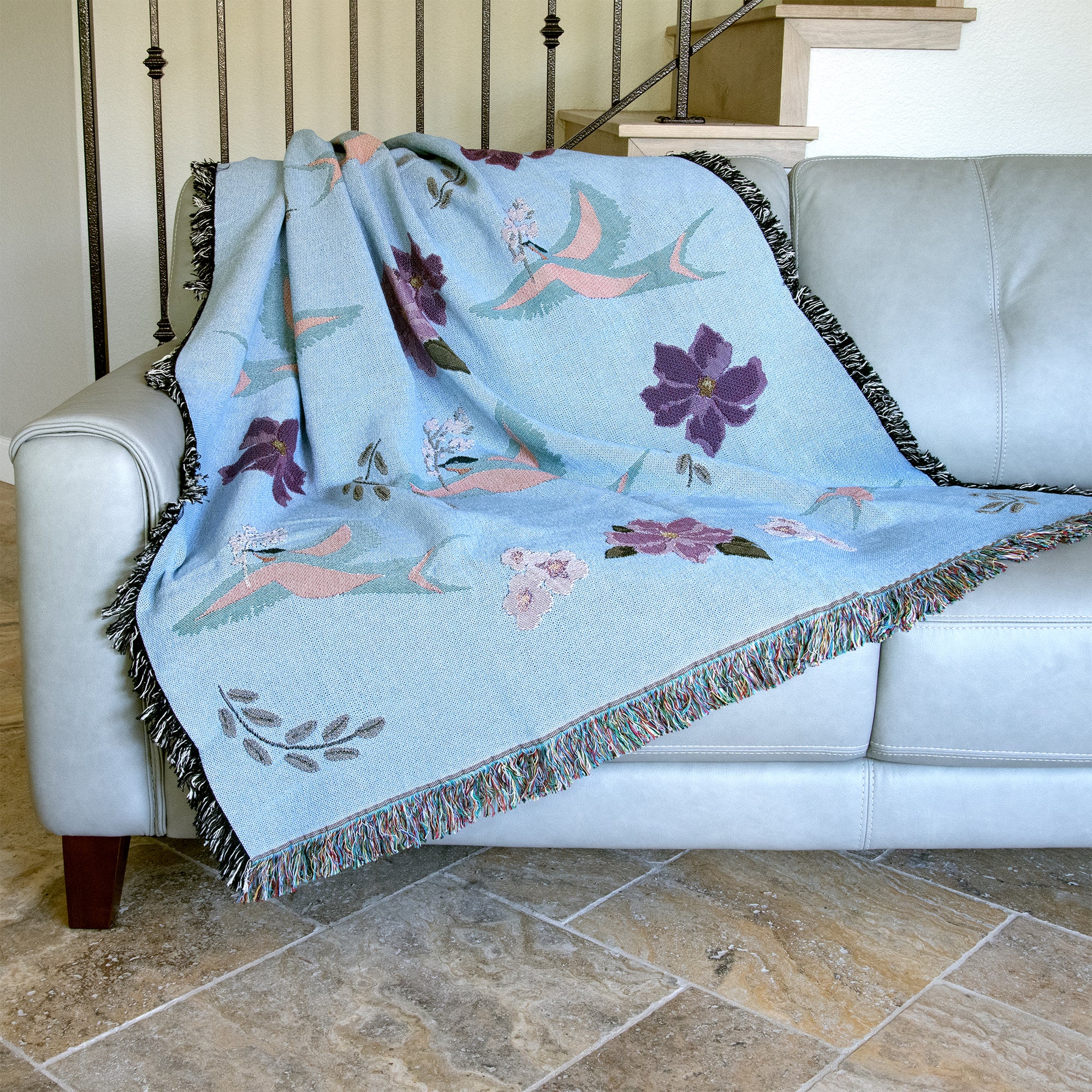 Decorative blanket with blue birds and flower pattern woven into a light blue background, draped over a sofa.
