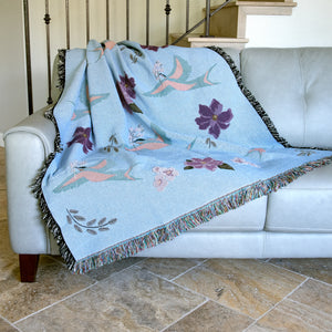 Decorative blanket with blue birds and flower pattern woven into a light blue background, draped over a sofa.