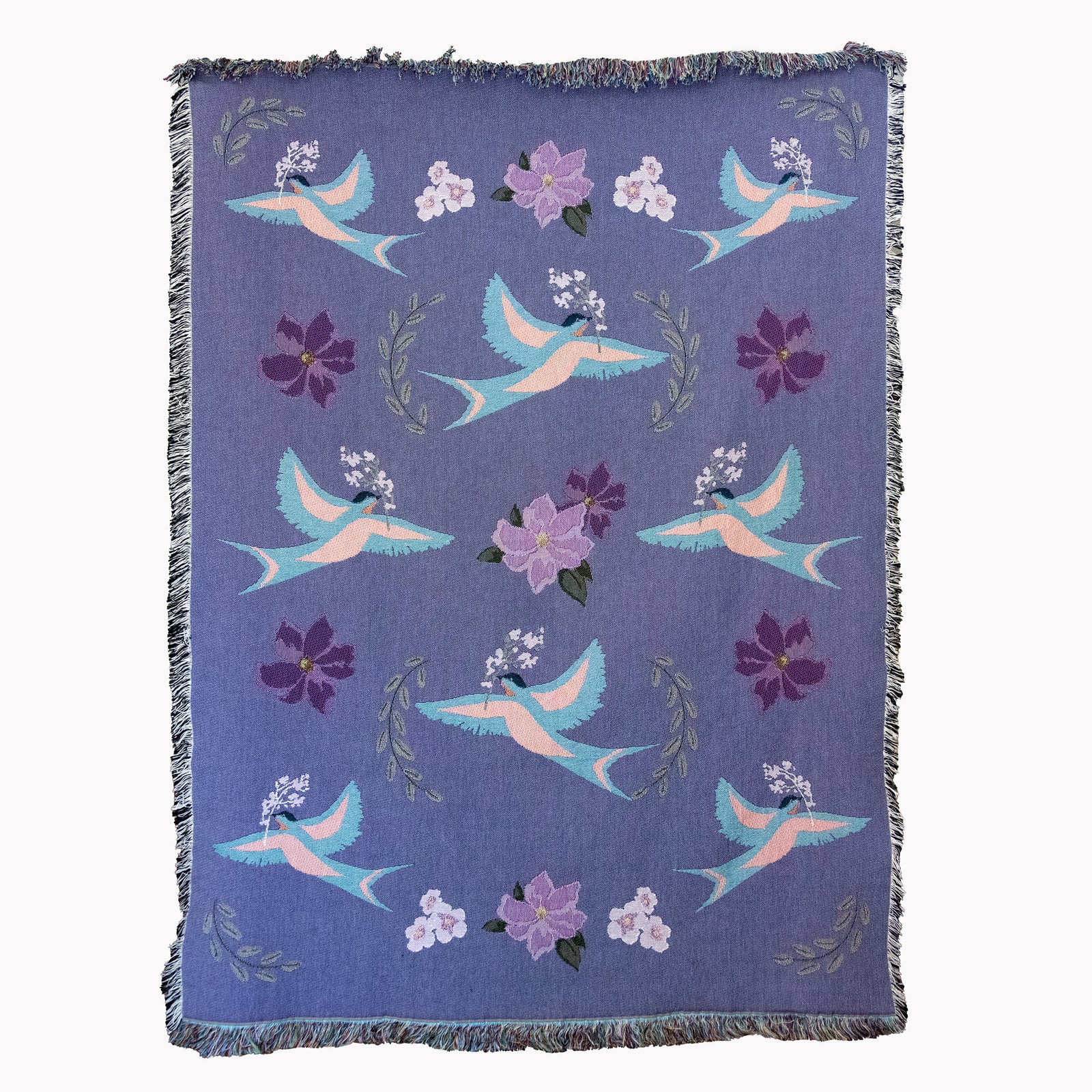 Decorative blanket with light blue birds and flower pattern woven into a purple background, with fringed edges.