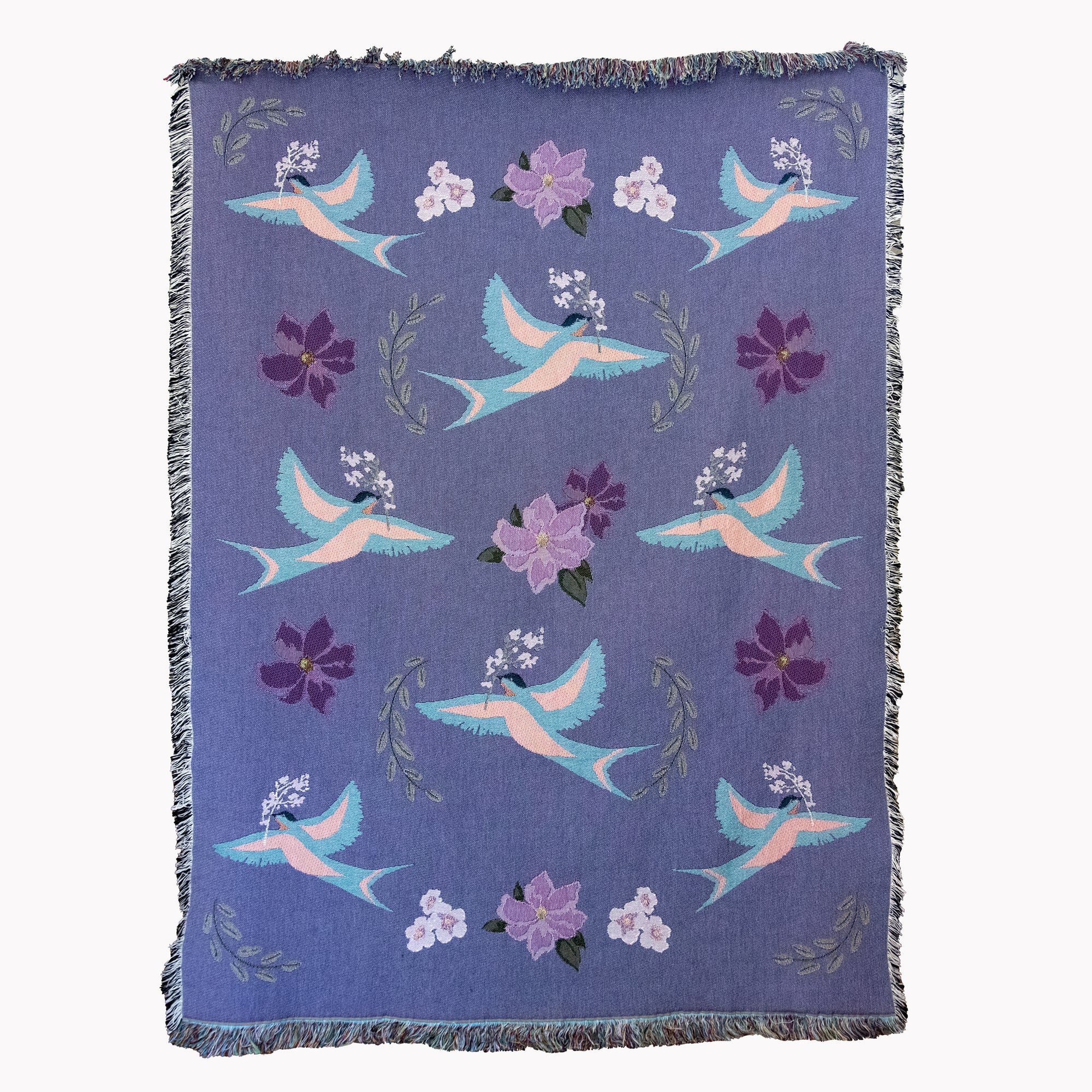 Decorative blanket with light blue birds and flower pattern woven into a purple background, with fringed edges.