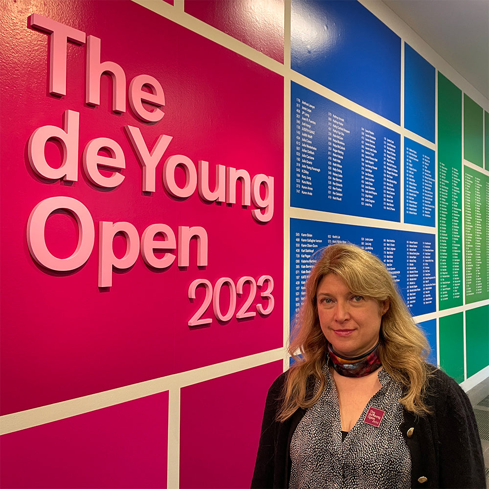 Participating artist Oksana Johnson  in front of multi-colored sign for de Young Open exhibition in San Francisco